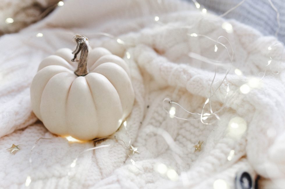 neutral fall colors decor featuring a white pumpkin, white knitted blanket, and fairy lights