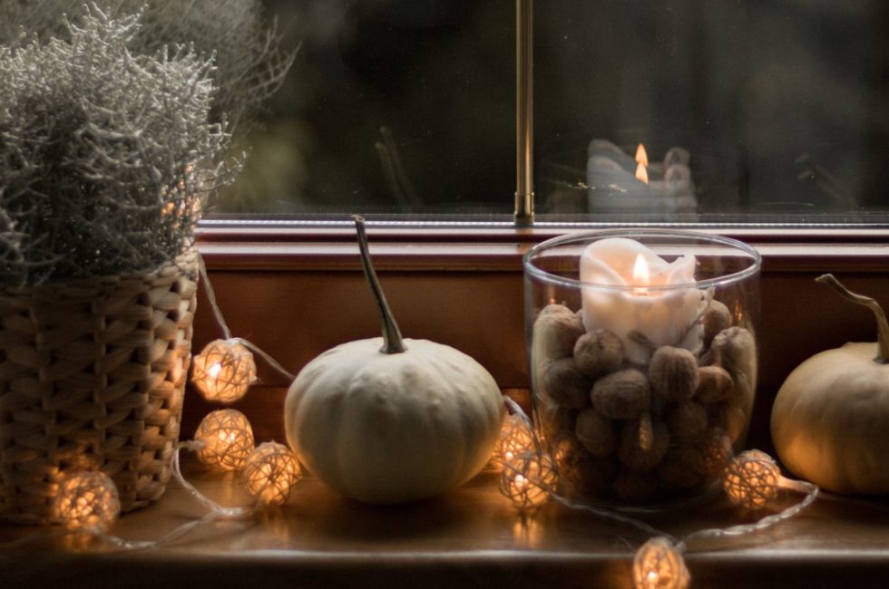 fall home decor featuring a small basket of herbs, a decorative candle arranged with walnuts, and light pumpkins on a windowsill