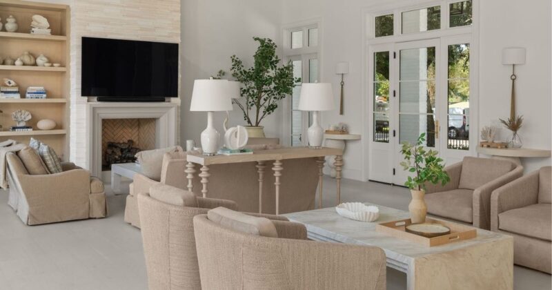 Florida style interior design living room with neutral beige sofas, chairs and bookshelf, with white floor walls and fireplace