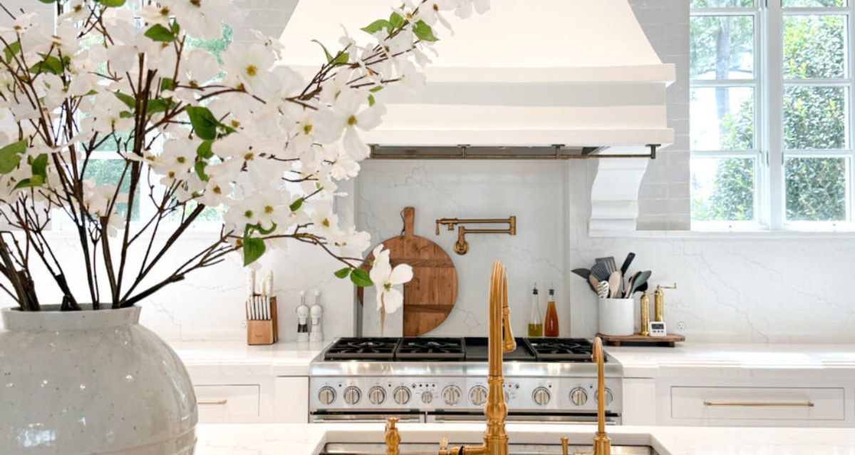 Natural light shining into a white kitchen with wooden and gold accessories that bring a natural element into the space